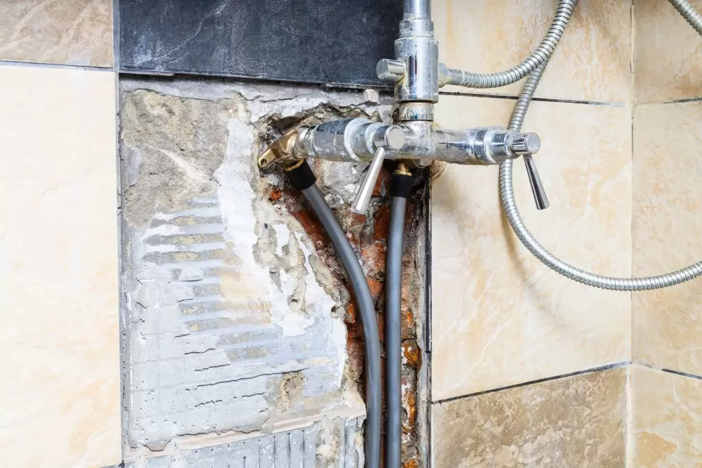 Corroded pipework behind a tiled wall from an undetected leak